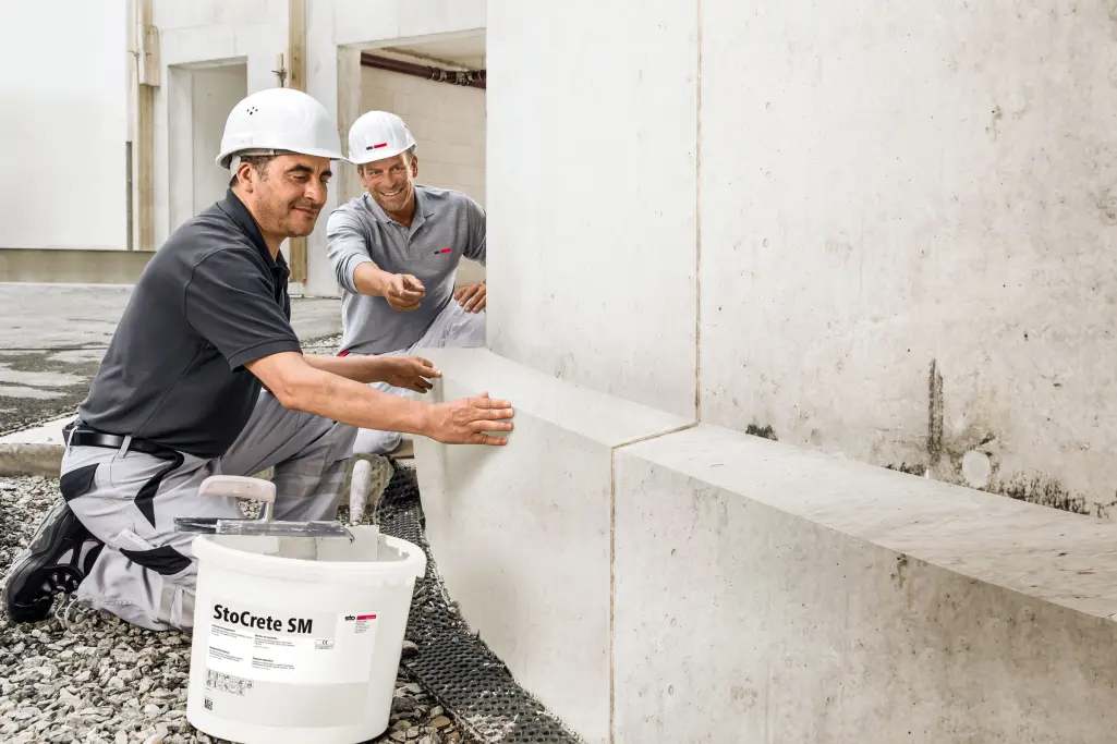 Applicators kneel in front of concrete facade