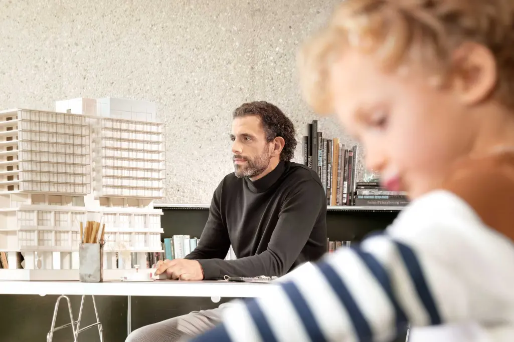 Blurred child playing in the foreground, father in the background, architect sitting at a desk.