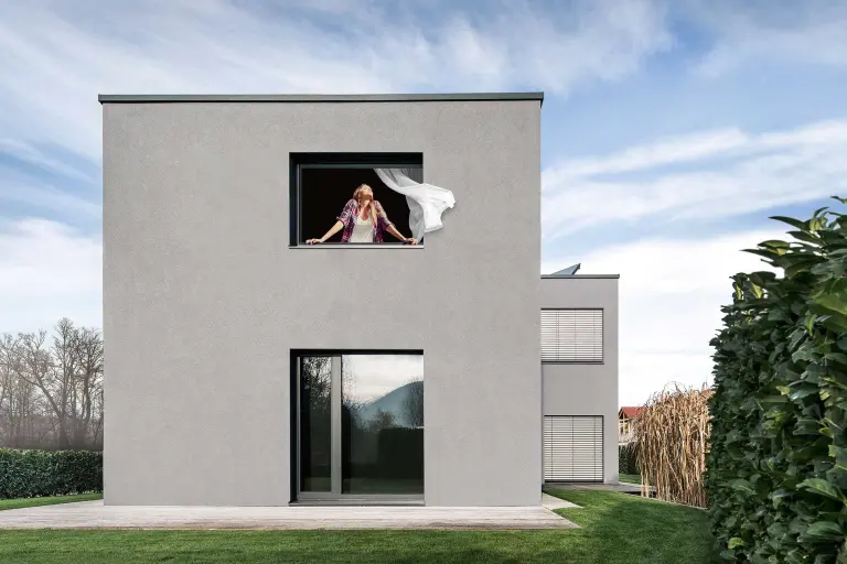 Woman looks out of a house with a grey Sto facade, breathing clean air thanks to StoColor Photosan