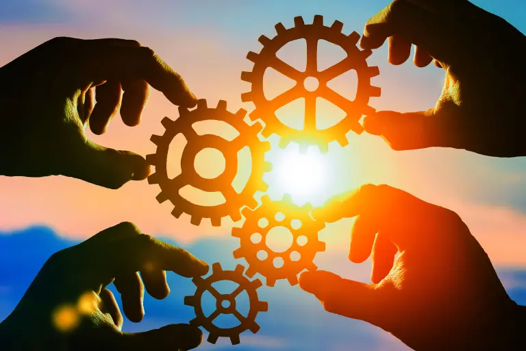 Tightly interlocked: 4 hands hold cogwheels against the sun, the sky