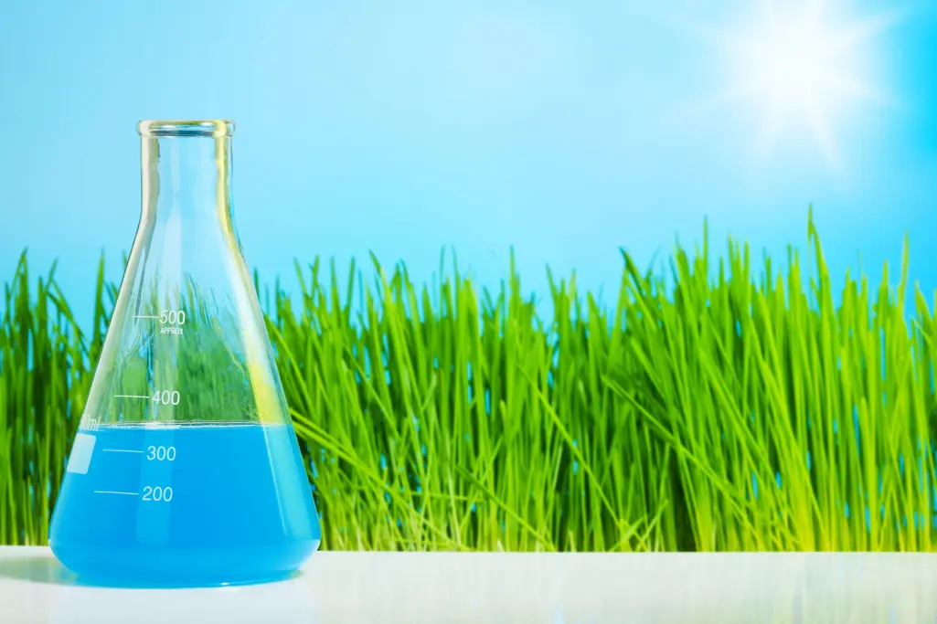 Test tube with blue liquid, chemical solution, green meadow behind, blue sky
