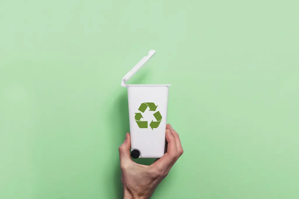 Hand holds white recycle dustbin against green background. Sustainability